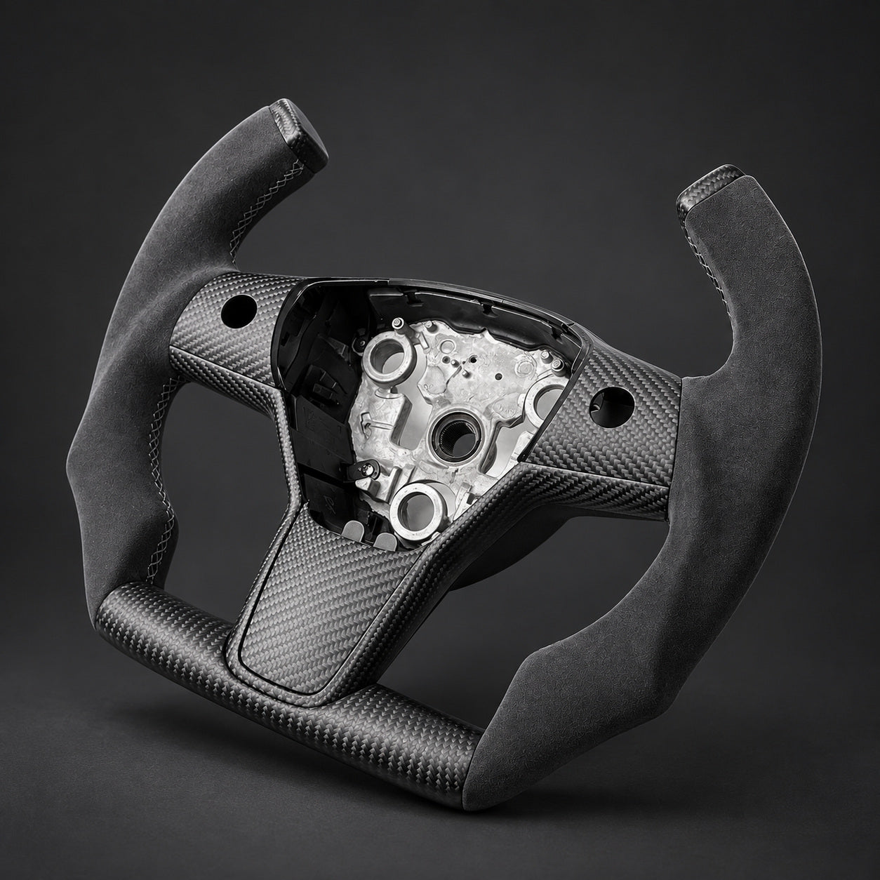 Open-top F1 wheel on graphite, showing Alcantara grips, carbon tip caps, flat carbon lower rim and the empty airbag mounting area.