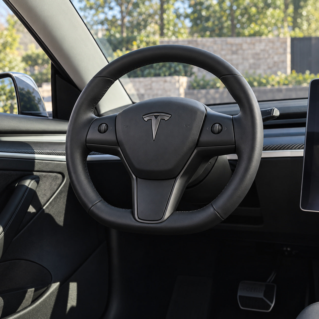 Same-angle appearance illustration of an original round black steering wheel in an earlier Model 3 or Model Y cabin.
